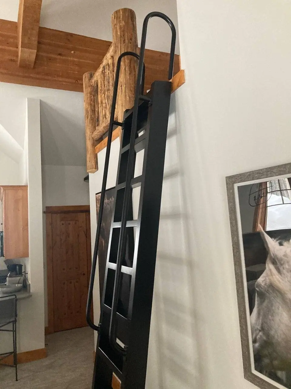 A black steel loft ladder mounted beside a rustic log beam
