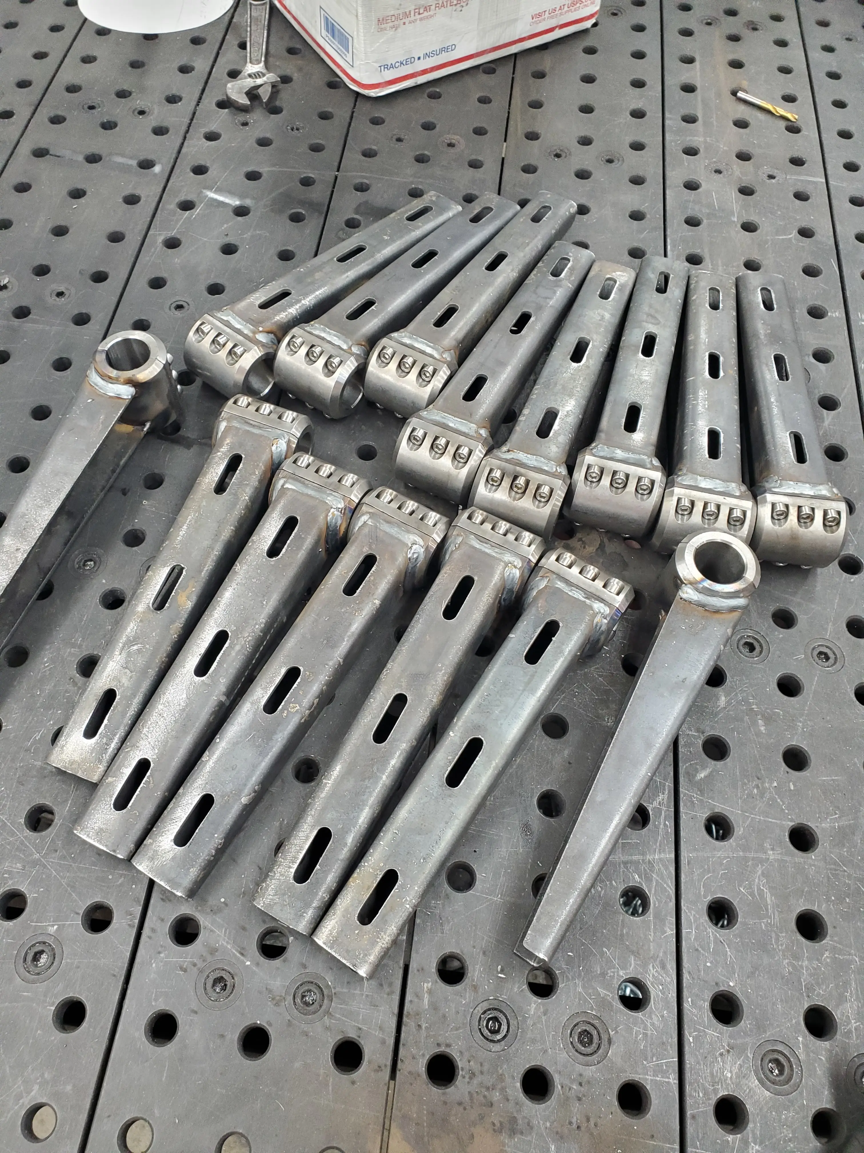 Machined steel brackets laid out on the welding table
