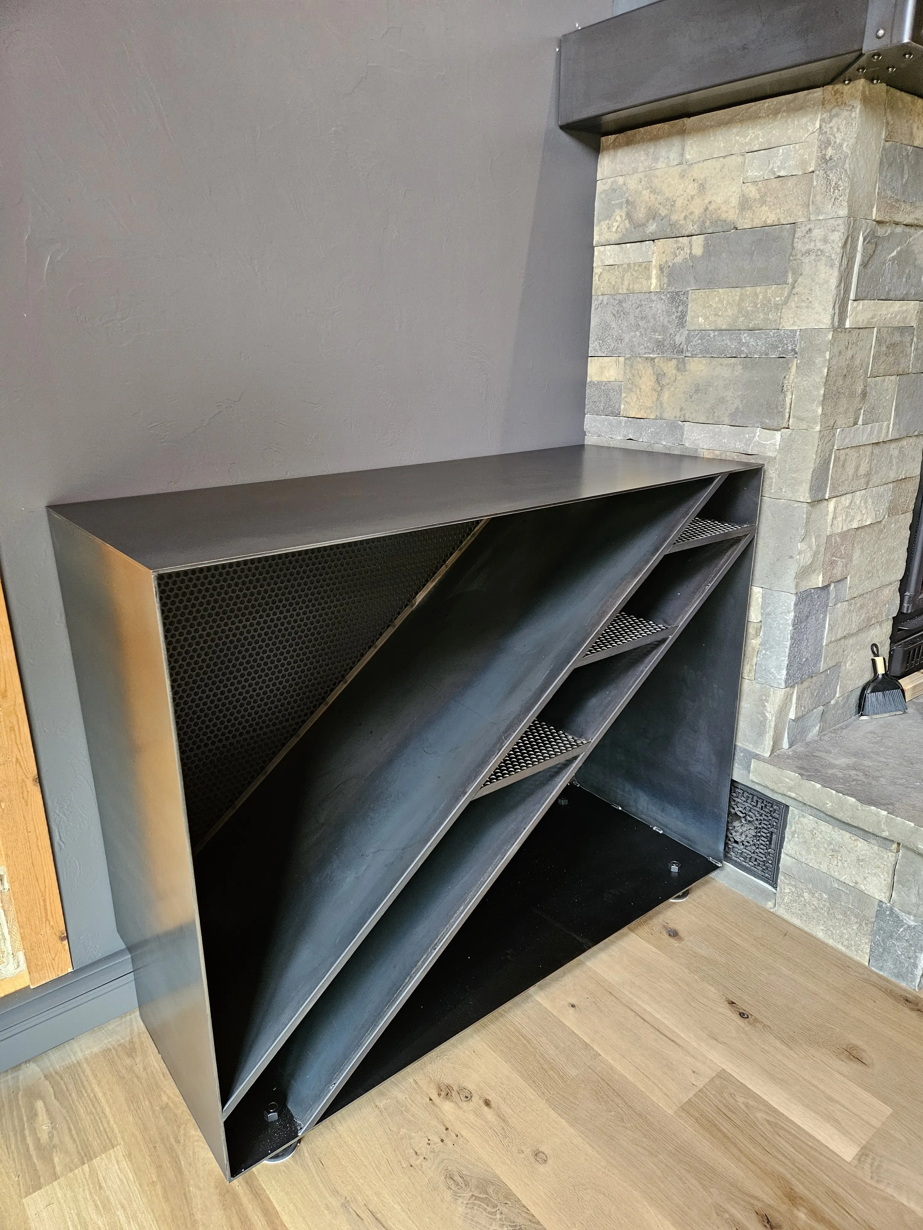 A one-off blackened-steel shelving unit built beside a stone fireplace