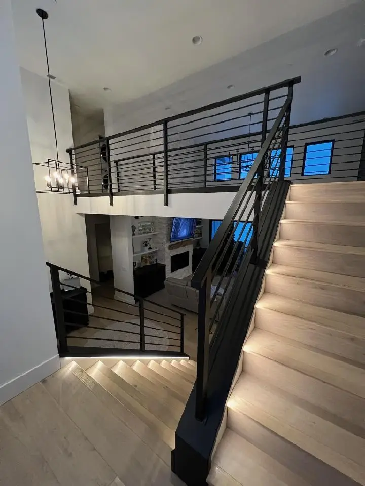 A split-level staircase at dusk with a black horizontal-bar railing and lit treads