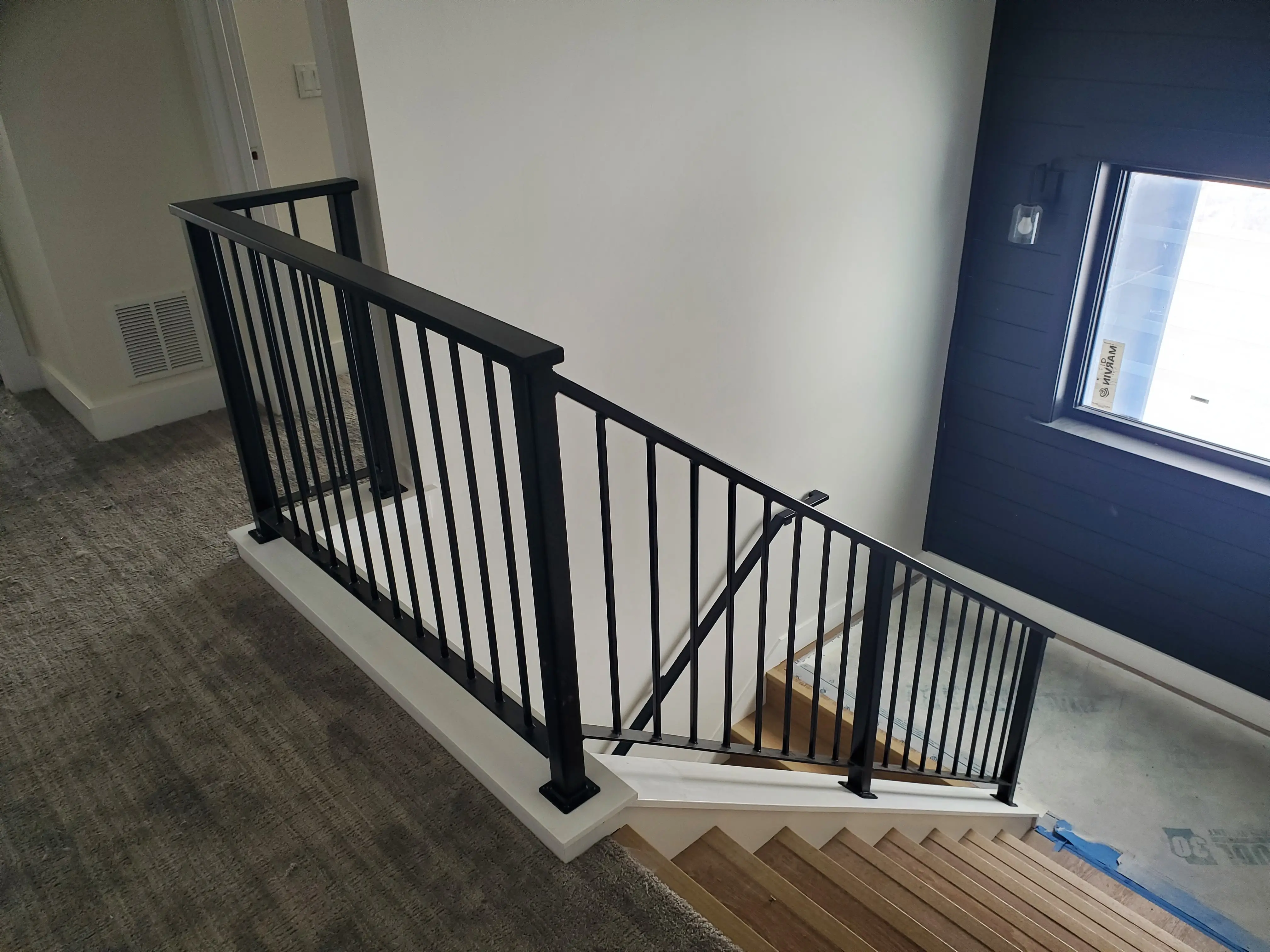An interior staircase with a black vertical-bar steel railing and a dark accent wall