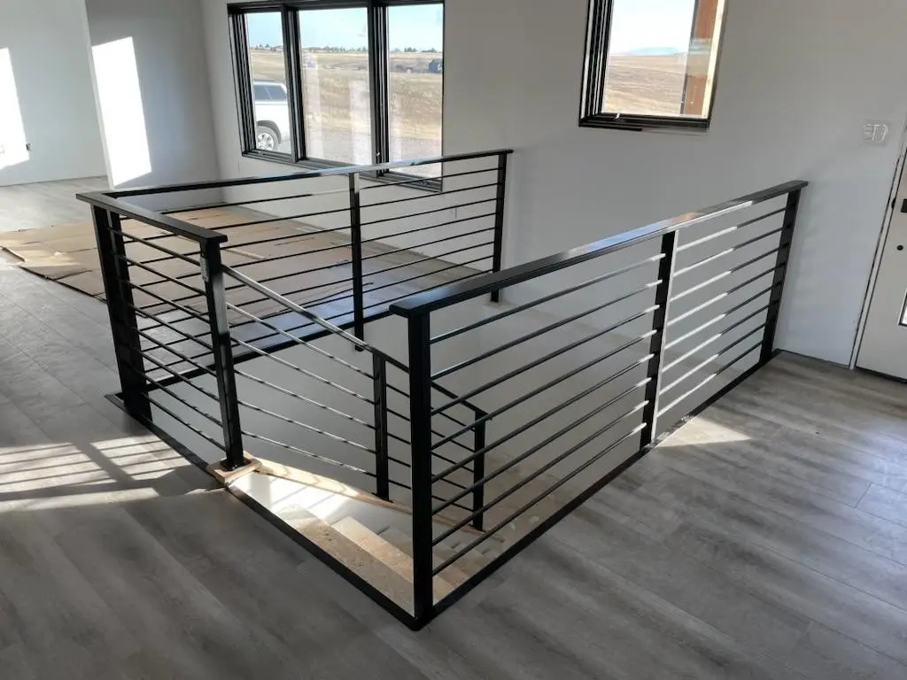 An L-shaped black horizontal-bar railing around a stairwell opening, with wide windows and mountain views